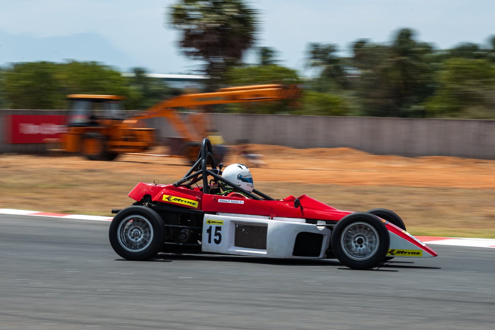 Senaajit racing his red number 15 car past the camera, background blurred by the panning shot