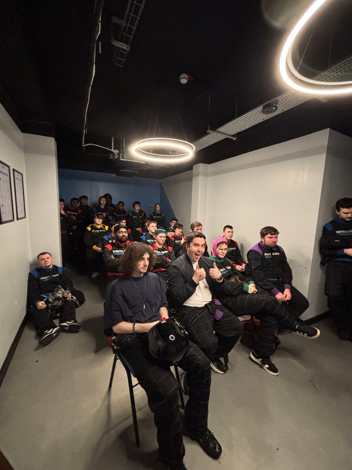 A room full of society members in race suits at a karting event briefing