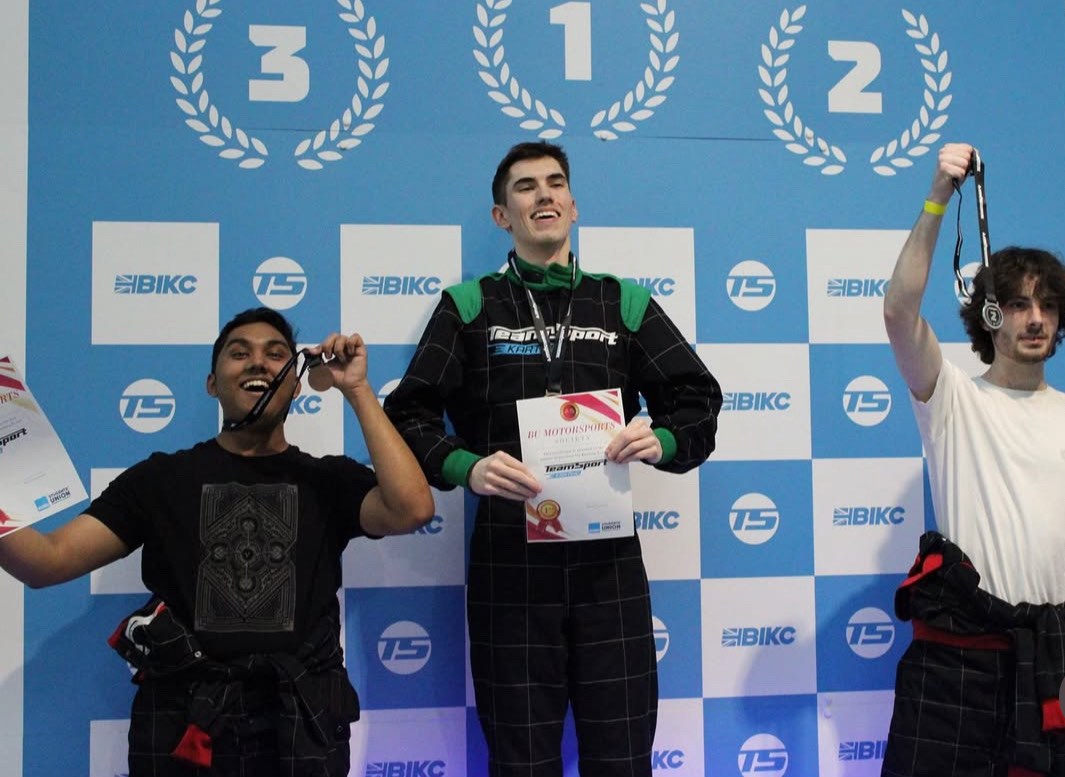 Three society members celebrating on the podium at a TeamSport karting race, holding medals and certificates